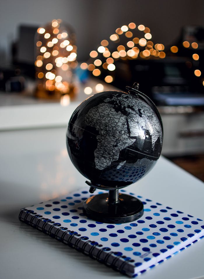Services-03 Elegant black globe and notebook against warm bokeh lights, perfect for educational themes.